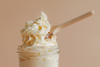 Whipped tallow cream inside glass skincare jar, smooth peaks with a wooden spoon