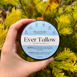 Hand holding a container of 'Ever Tallow' Beard Balm against a green foliage background