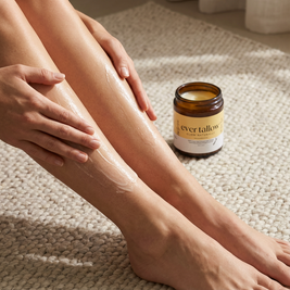 Person applying cream to their leg with a jar of 'ever tallow' cream on a textured surface.