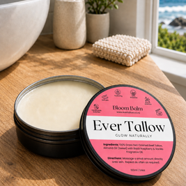 An open tin of Ever Tallow Glow on a wooden bathroom counter beside a sink, soap dispenser, plant, and a window view of the ocean. 