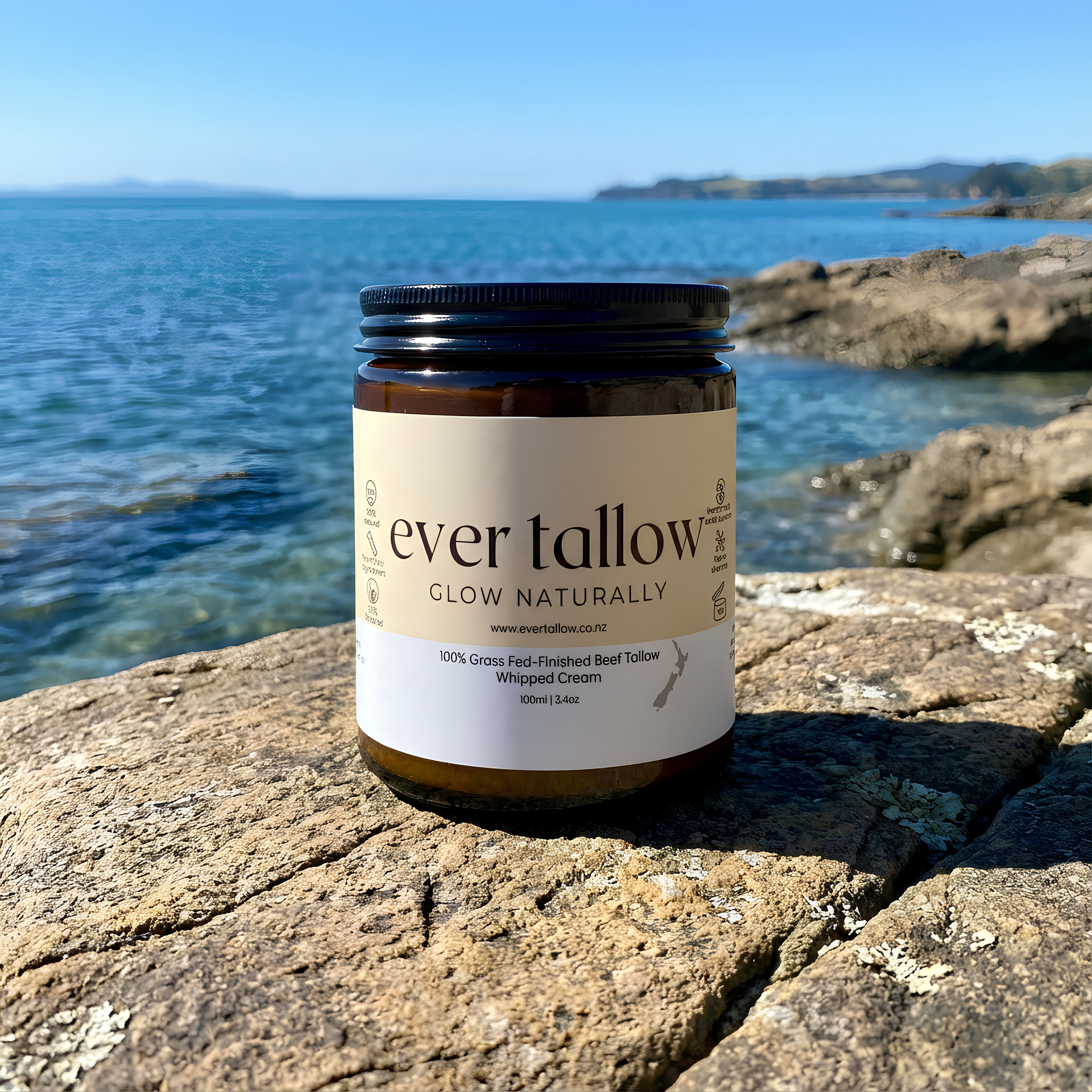 Jar of 'bare tallow' cream on a rock with ocean and sky in the background