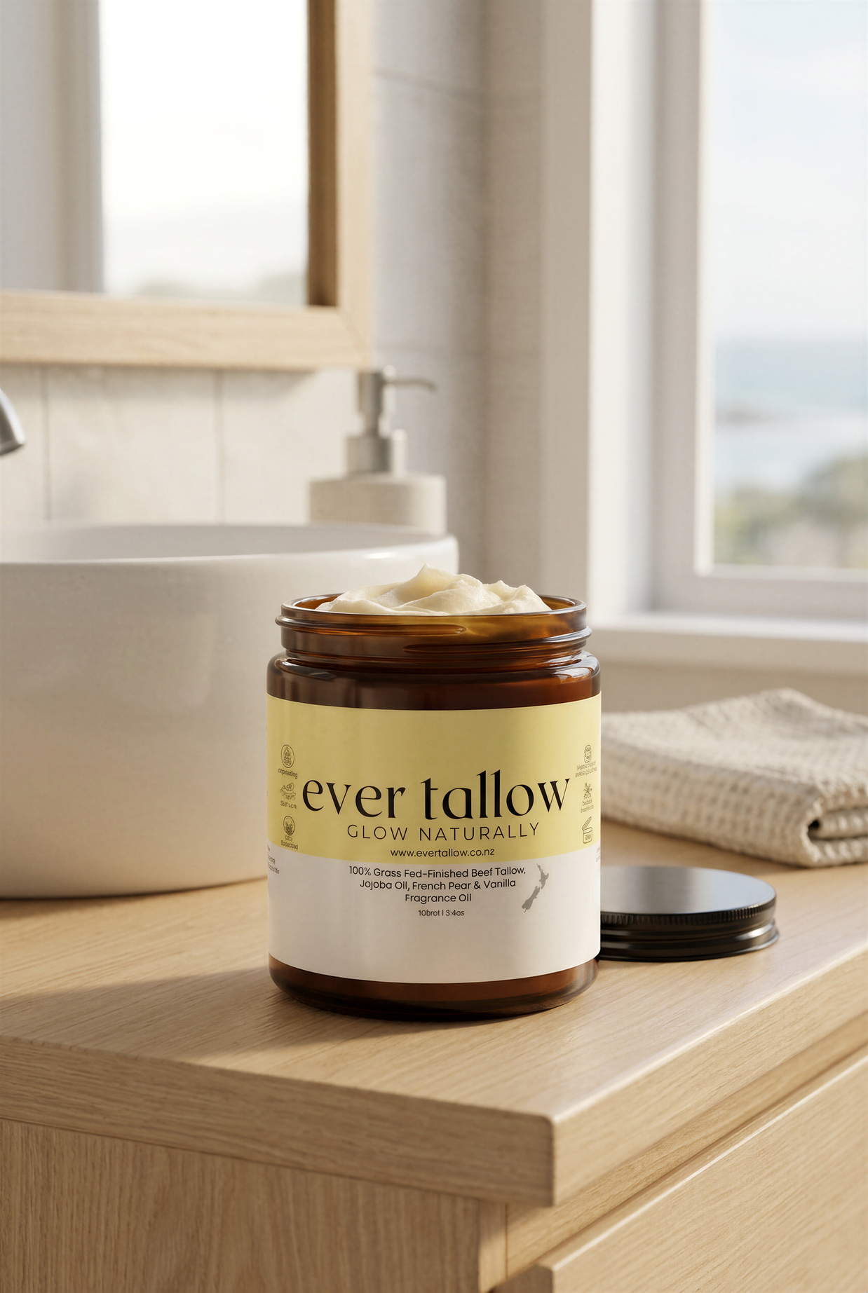 A jar of Ever Tallow Glow Naturally French Pear and Vanilla butter sits on a light wood vanity counter in a bright bathroom setting, with its lid placed beside it.