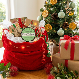 Red gift bag with 'Ever Tallow' product in front of a decorated Christmas tree.