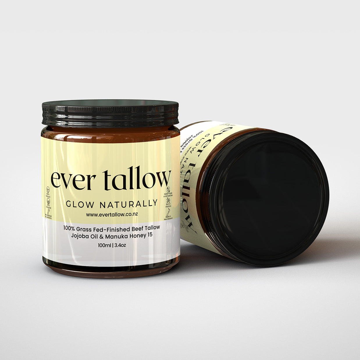 Two jars of Two jars of tallow cream manuka honey. One jar is on its side.