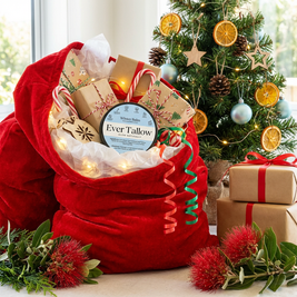 Red gift bag filled with Christmas-themed items in front of a decorated tree.